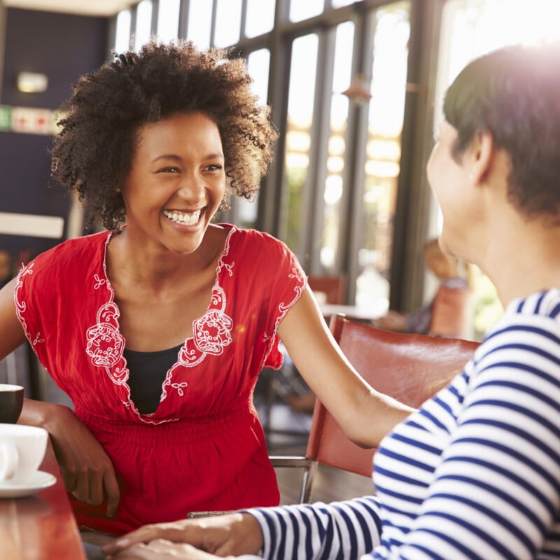 two women smiling and laughing at a sunny coffee shop
